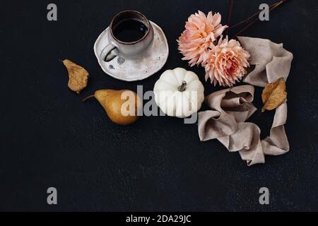 Herbst Stillleben Zusammensetzung. Tasse Kaffee, Birnenfrucht und weiße Kürbisse mit rosa Dahlienblüten. Schwarzer Tabellenhintergrund. Buchenblätter. Moody Fall Stockfoto