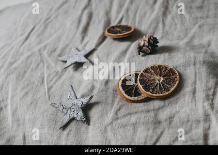 Weihnachten neutral Stillleben Komposition. Birkenrindensterne, Lärchenzapfen und trockene Orangenscheiben auf grauem Leinentischtuch Hintergrund. Moody Winter Stockfoto