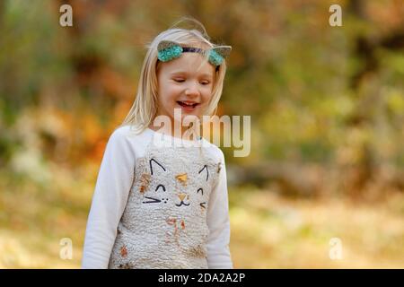 Ziemlich blonde junge Mädchen lachen im Freien an einem schönen sonnigen Herbsttag. Das Mädchen trägt Katze Stirnband und Katze Pullover. Stockfoto