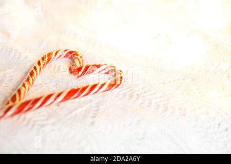 Weihnachts-Zuckerrohr gestreifter Weihnachtsmann in Herzform auf einer weißen Strickdecke. Ein Symbol der Liebe, ein Geschenk an einen geliebten Menschen, ein süßer Leckerbissen. Neujahr. Stockfoto