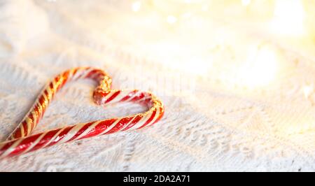 Weihnachts-Zuckerrohr gestreifter Weihnachtsmann in Herzform auf einer weißen Strickdecke. Ein Symbol der Liebe, ein Geschenk an einen geliebten Menschen, ein süßer Leckerbissen. Neujahr. Stockfoto