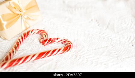 Weihnachts-Zuckerrohr gestreifter Weihnachtsmann in Herzform auf einer weißen Strickdecke. Ein Symbol der Liebe, ein Geschenk an einen geliebten Menschen, ein süßer Leckerbissen. Neujahr. Stockfoto
