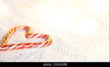 Weihnachts-Zuckerrohr gestreifter Weihnachtsmann in Herzform auf einer weißen Strickdecke. Ein Symbol der Liebe, ein Geschenk an einen geliebten Menschen, ein süßer Leckerbissen. Neujahr. Stockfoto