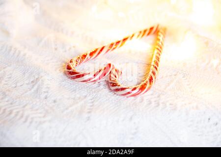 Weihnachts-Zuckerrohr gestreifter Weihnachtsmann in Herzform auf einer weißen Strickdecke. Ein Symbol der Liebe, ein Geschenk an einen geliebten Menschen, ein süßer Leckerbissen. Neujahr. Stockfoto