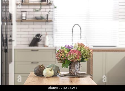 Herbstkomposition von Blumen von Hortensien und Kürbissen auf dem Hintergrund des Innenraums einer hellen modernen Küche. Stockfoto