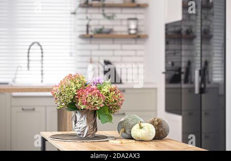 Herbstkomposition von Blumen von Hortensien und Kürbissen auf dem Hintergrund des Innenraums einer hellen modernen Küche. Stockfoto