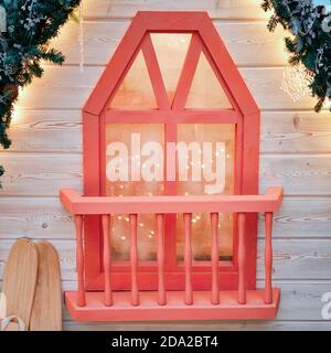 Balkon mit einem Fenster eines Holzhauses mit Zweigen eines Weihnachtsbaums mit Zapfen und Girlanden geschmückt. Ornament für die Feier des neuen Jahres Stockfoto