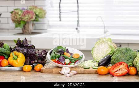 Frisches Gemüse in den Prozess der Zubereitung von Salat auf einem Holztisch vor dem Hintergrund einer modernen Küche Innenraum Kopie Raum. Stockfoto