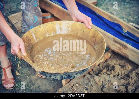 Damenhände mit einem Tablett für die Gewinnung von Goldsand in den USA. Frau Goldgräber im amerikanischen Wilden Westen. Waschen von Sand in Wasser, um kostbare zu erhalten Stockfoto