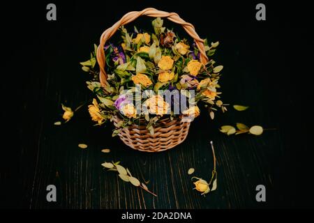 Getrocknete Blumen auf einem schwarzen Hintergrund aus Holz. Trockener Rosenstrauß in einem Weidenkorb. Schöne verwelkt Blumen mit gefallenen Blättern auf einem schwarzen Tisch. Stockfoto