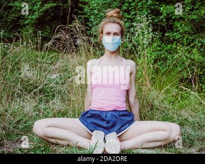 Ein Mädchen in einer Maske sitzt in der Natur und verbreitet sie Knie an den Seiten Stockfoto