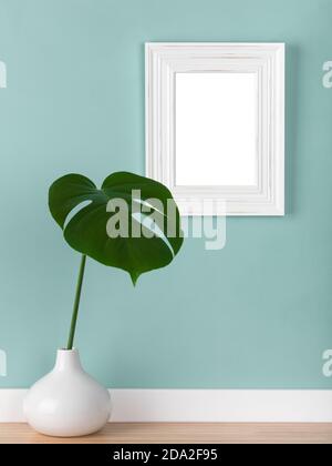 Vertikaler Shabby White Bilderrahmen-Mockup mit Monstera deliciosa Blatt in Vase vor stummen grünen Wand. Leerer Bildbereich mit Beschneidungspfad maskiert Stockfoto