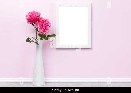Weißer vertikaler Bilderrahmen, Seitenverhältnis von 3x4, auf rosa Wand und Rosen in Vase Mockup Vorlage. Leerer Bildbereich isoliert mit Beschneidungspfad Stockfoto