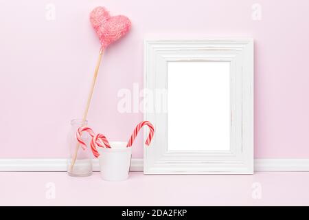 Weißer vertikaler Bilderrahmen, Seitenverhältnis für EINE Größe, Mockup-Vorlage. Glas mit Zuckerstöcken und herzförmigem Ornament vor rosa Wand. Leer Stockfoto