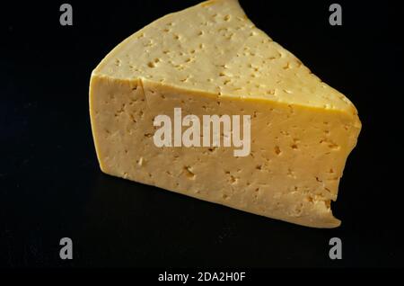 Stück Hartkäse auf schwarzem Hintergrund. Ein großes dreieckiges Stück echten Käses. Produkte, Zutaten. Stockfoto