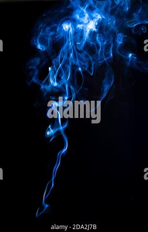 Rinnsal von Vape Rauch isoliert auf schwarzem Hintergrund. Rauchwirbel mit blauer Hintergrundbeleuchtung, vertikale Fotografie für Design Stockfoto