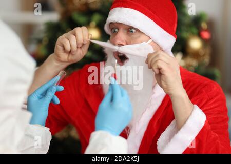 Arzt in Schutzanzug unter Abstrich pcr von santa claus In der Nähe von Weihnachtsbaum Stockfoto