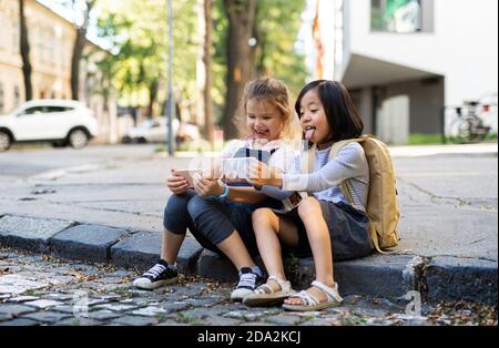 Kleine Mädchen mit Smartphones sitzen im Freien in der Stadt, Selfie zu nehmen. Stockfoto