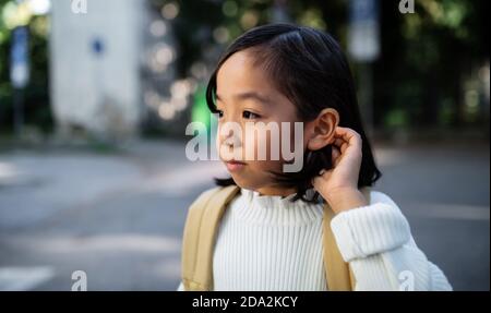 Portrait von kleinen japanischen Mädchen mit Rucksack zu Fuß im Freien in der Stadt. Speicherplatz kopieren. Stockfoto