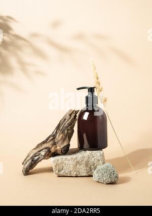 Steinpodium und braune Kosmetikflasche in kreativer natürlicher Komposition auf beigem Hintergrund mit Pflanzenschatten. Speicherplatz kopieren. Vorderansicht Stockfoto