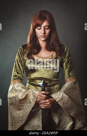Schöne rote Haare Frau posiert mit grünen mittelalterlichen Kleid und Schwert Stockfoto