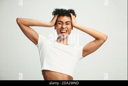 Homosexuell Mann suchen aufgeregt. Geschlecht Flüssigkeit Mann trägt Crop Top lachend mit seinen Händen im Haar vor weißem Hintergrund. Stockfoto