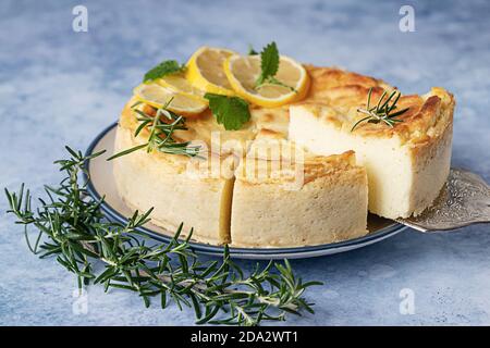 Käsekuchen mit Zitronenvanille, verziert mit Rosmarin-, Minze- und Zitronenscheiben. Ricotta keine Kruste Käsekuchen oder Kasserolle. Blauer Betonhintergrund. Stockfoto