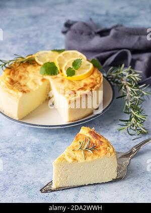 Käsekuchen mit Zitronenvanille, verziert mit Rosmarin-, Minze- und Zitronenscheiben. Ricotta keine Kruste Käsekuchen oder Kasserolle. Blauer Betonhintergrund. Stockfoto