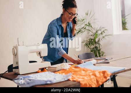 Schneiderin, die zu Hause eine Bestellung von Masken erhält. Frau, die zu Hause arbeitet und mit ihrem Kunden telefoniert. Stockfoto