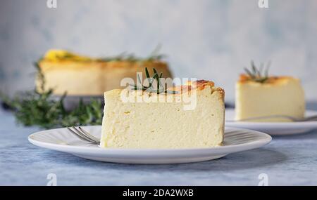 Käsekuchen mit Zitronenvanille, verziert mit Rosmarin-, Minze- und Zitronenscheiben. Ricotta keine Kruste Käsekuchen oder Kasserolle. Blauer Betonhintergrund. Stockfoto