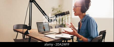 Frau, die ihren Podcast von zu Hause aus ausstrahlte. Frau mit Kopfhörern, die von zu Hause aus in ein Mikrofon spricht. Stockfoto