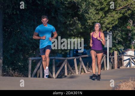 Junger Mann in blauem T-Shirt und junge Frau in lila t-Shirt Joggen im Park Stockfoto