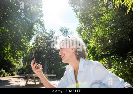 Seitenportrait lächelnde ältere Frau, die im Park auf das Handy schaut Stockfoto