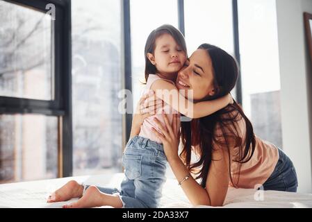 Junge Mutter mit ihrer Tochter umarmt sich gegenseitig auf dem Bett Stockfoto