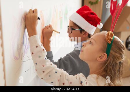 Seitenansicht Porträt von Jungen und Mädchen Zeichnung an den Wänden, während das Tragen von Santa Hüte und Geweih für Weihnachten, kopieren Raum Stockfoto