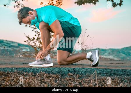 Porträt eines jungen Mannes im Park, der die Schnürsenkel bindet Von ihren Sneakers trägt eine Gesichtsmask Stockfoto