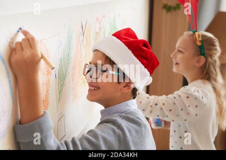 Seitenansicht Porträt von Jungen und Mädchen Zeichnung an den Wänden, während das Tragen von Santa Hüte für Weihnachten, kopieren Raum Stockfoto