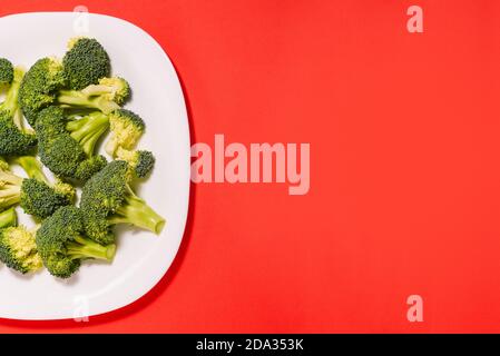 Brokkoli in einer weißen Platte auf einem roten Hintergrund mit Kopierraum. Reifes Gemüse, Kohl Nahaufnahme. Ernährung, Ernährung und Gewichtsverlust Konzept Stockfoto