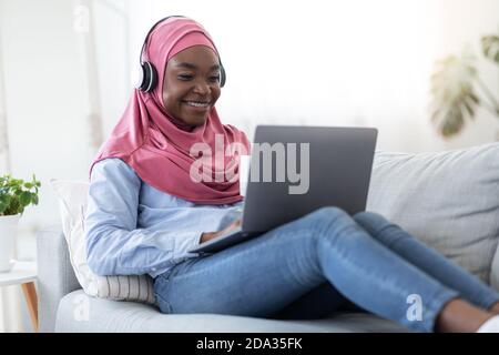 Zeitvertreib Zu Hause. Schwarze Muslimische Frau In Hijab Entspannung Mit Laptop Und Kaffee Stockfoto