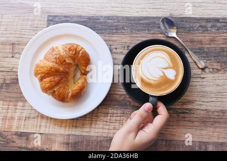 Kaffee und Croissant auf Holztisch, Blick von oben. Stockfoto