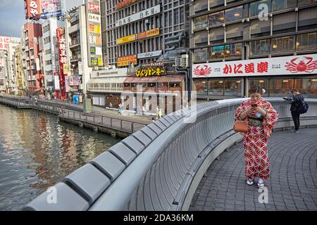 Osaka, Japan, April 2018. Eine traditionell gekleidete Frau, die ihr Mobiltelefon auf der Ebisu-Brücke von Dontonbori anschaut. Stockfoto