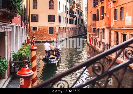 Venezianische Gondoliere nimmt Touristen mit auf Gondelfahrt durch den ruhigen schmalen Kanal durch Venedig, romantische Reise Stockfoto