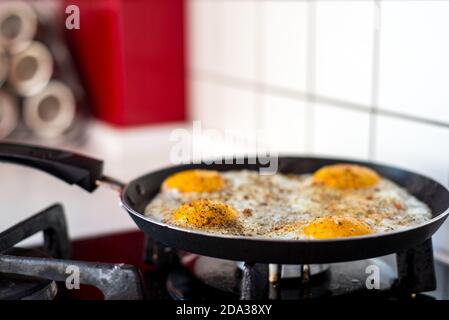 Vorbereitung eines englischen Frühstücks. Vier zerbrochene Eier in einer Pfanne auf dem Herd. Tisch und Bratpfanne. küchengeräte Stockfoto