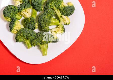 Brokkoli aus nächster Nähe. Frischer Brokkoli auf einem Teller auf rotem Hintergrund. Gesunde und diätetische Lebensmittel. Vegetarische Rezepte Stockfoto