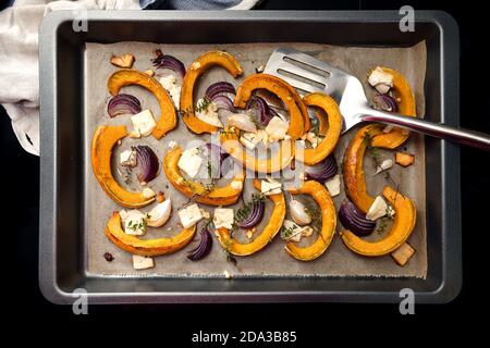 Gebackene Kürbis- oder Kürbisscheiben mit roten Zwiebeln, Knoblauch, Feta-Käse und Thymian auf einem Backblech, Mahlzeit aus Herbstgemüse für Thanksgiving und Hallo Stockfoto