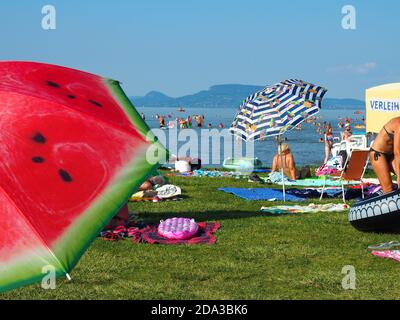 Balatonmáriafürdő, UNGARN - Jul 31, 2020: Bunte Sonnenschirme, Sonnenbaden und Baden Menschen am Strand des Plattensees, Ungarn in heißen Julitag Stockfoto