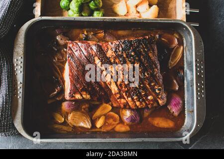 Rustikales Schweinebraten mit gebratenem Schweinebauch und Kruste Serviert in einer Kasserolle mit roten Zwiebeln Stockfoto