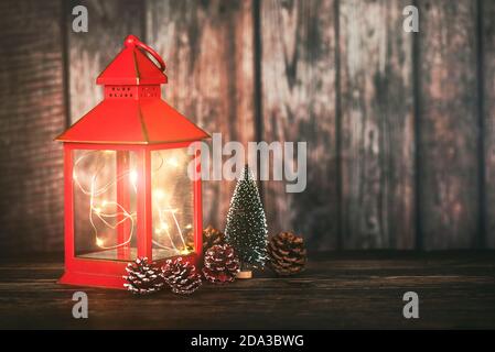 Frohe Weihnachten.Weihnachtskonzept Hintergrund.Rote Weihnachtslaterne mit weihnachtsbaum und Tannenzapfen über Holztisch Stockfoto