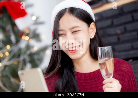 Junge asiatische Frau Selfie Video-Anruf online mit Freunden und zeigen Glas in Weihnachten am Telefon zu Hause mit sozialen Distanzierung, neue normale, weibliche vi Stockfoto