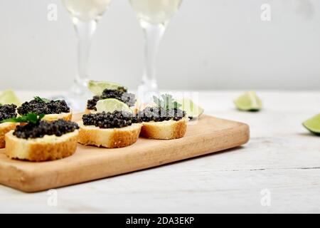 Stör schwarzer Kaviar in Holzschale, Sandwiches und Champagner auf weißem Hintergrund Kopierraum. Stockfoto